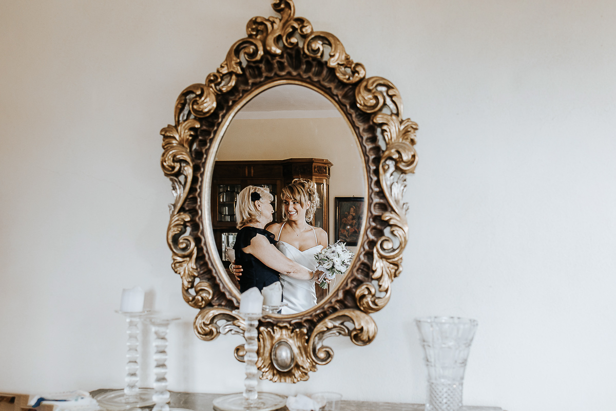 Matrimonio a Villa Delfini di Morsasco (AL) nel Monferrato. Preparazione dell a sposa. mamma abbraccia la sposa allo specchio.