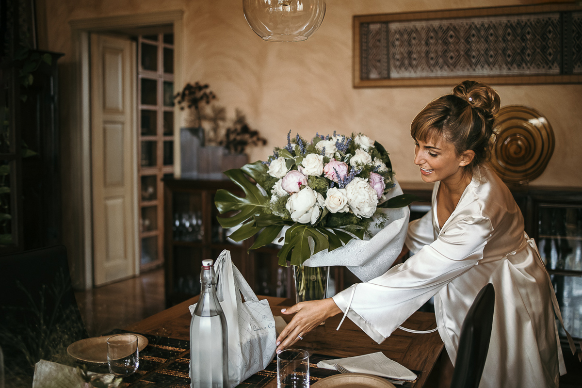 Matrimonio a Torino in un palazzo storico di Piazza Statuto. Preparazione della sposa. Sposa che sposta un pacchetto sulla tavola apparecchiata vicino ad un mazzo di fiori bianchi.