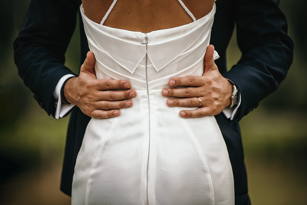 Matrimonio a Villa Delfini di Morsasco (AL) nel Monferrato. Ritratto degli sposi in mezzo alle vigne. Dettaglio sulle mani dello sposo che cinge la vita della sposa.