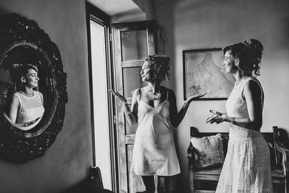 Matrimonio a Villa Delfini di Morsasco (AL) nel Monferrato. Preparazione dell a sposa. damigella d'onore con un'espressione buffa e sposa che si riflette nello specchio.