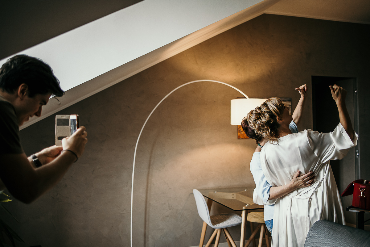 Matrimonio a Torino in un palazzo storico di Piazza Statuto. Preparazione della sposa. Sposa con la truccatrice. Fratello della sposa le fotografa.