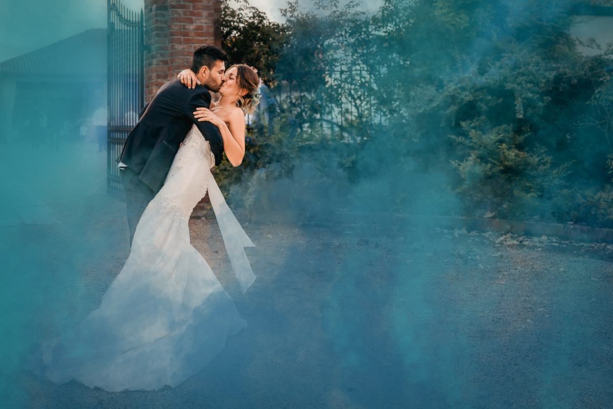Matrimonio a Villa Fiorita ad Asti. Ricevimento. Sposi che si baciano in mezzo ai fumogeni colorati