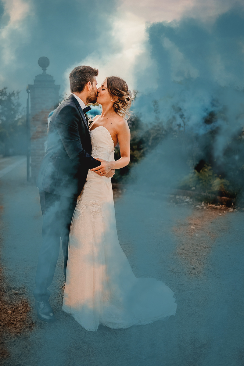 Matrimonio a Villa Fiorita ad Asti. Ricevimento. Sposi che si baciano in mezzo ai fumogeni colorati