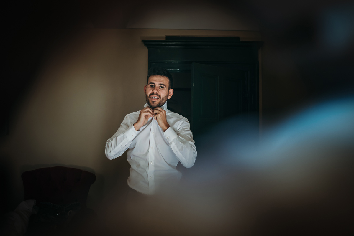 Matrimonio a Villa Fiorita ad Asti. Preparazione dello sposo.Sposo che si sistema il colletto della camicia