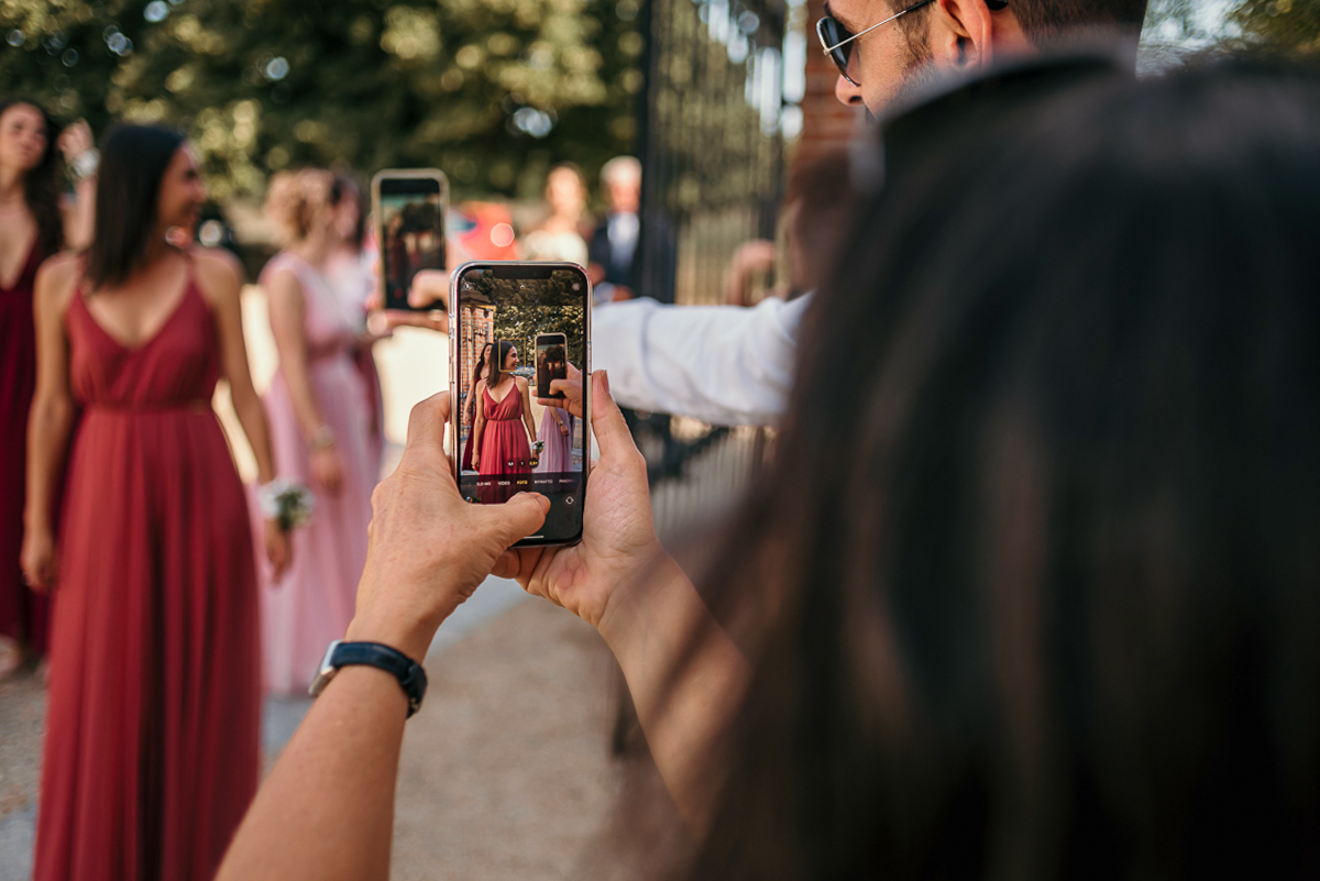 Matrimonio a Villa Fiorita ad Asti. Cerimonia.Invitata che scatta una foto con il cellulare al corteo nuziale.