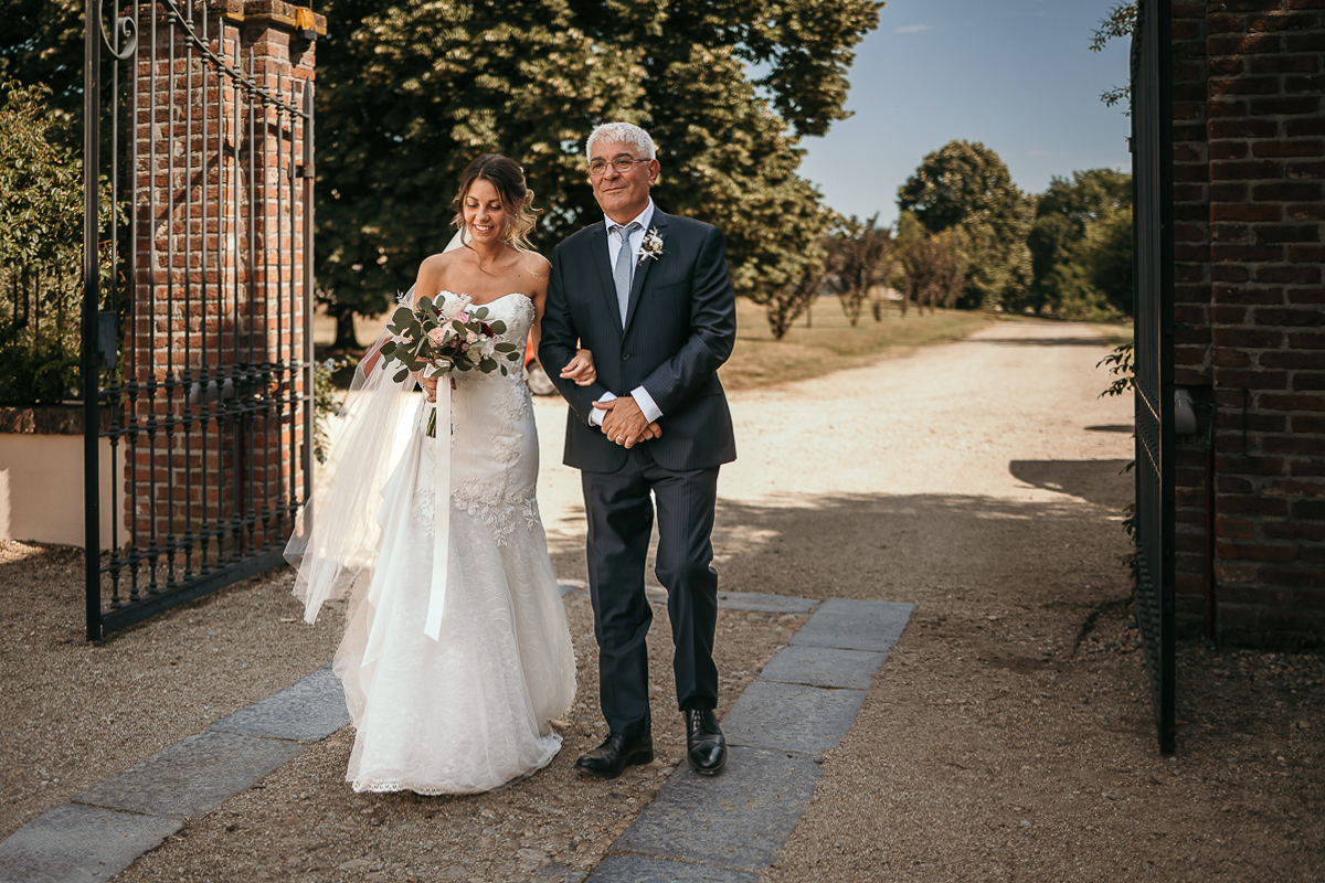 Matrimonio a Villa Fiorita ad Asti. Cerimonia.Sposa che entra con il padre.
