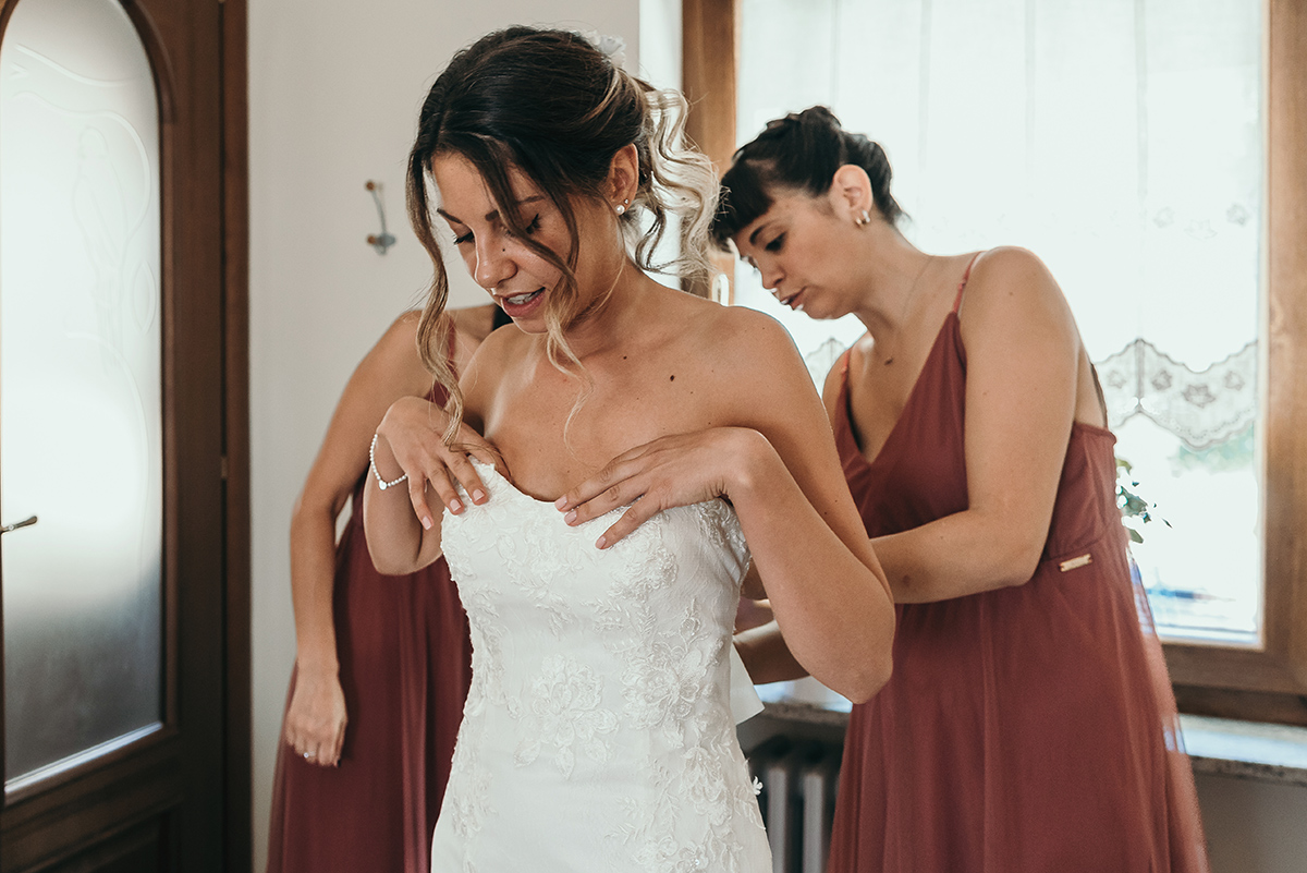 Matrimonio a Villa Fiorita ad Asti. Preparazione della sposa. Damigelle che chiudono l'abito della sposa