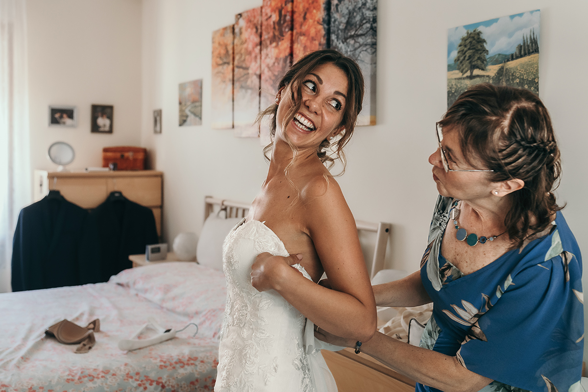 Matrimonio a Villa Fiorita ad Asti. Preparazione della sposa.Sposa che guarda la mamma che le abbottona l'abito