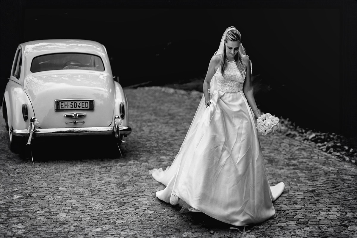 Villa Sassi matrimonio di Giulia e Nicolò. Ritratto della sposa davanti all'auto d'epoca bianca. Bianco e nero.