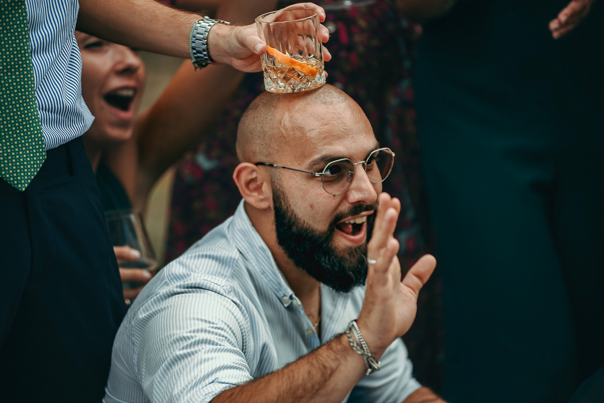 Villa Sassi matrimonio di Giulia e Nicolò. Aperitivo.Foto di gruppo. dettaglio di un bicchiere posto sul capo di un ragazzo.