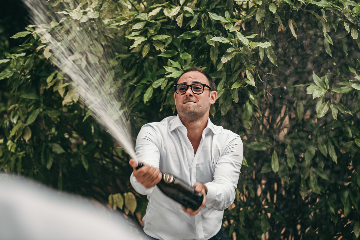 Villa Sassi matrimonio di Giulia e Nicolò. Aperitivo.Sposo spruzza gli amici con una bottiglia di vino.