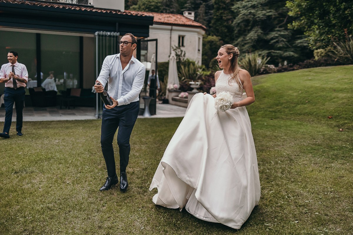 Villa Sassi matrimonio di Giulia e Nicolò. Aperitivo. Sposi che si dirigono verso il loro tavolo per la cena, ma sposo che si diverte a spruzzare di vino gli amici.