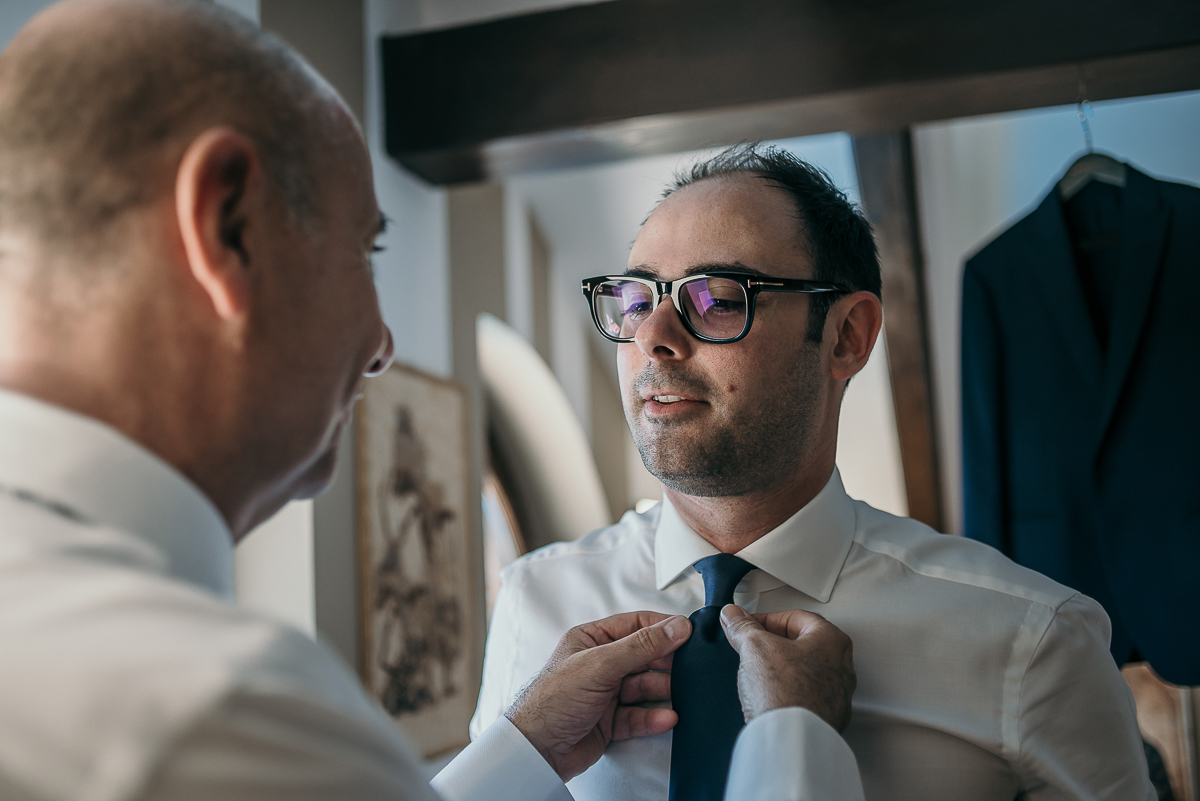 Matrimonio a Villa Sassi. Preparazione dello sposo a Baldissero Torinese. Padre sistema la cravatta dello sposo.