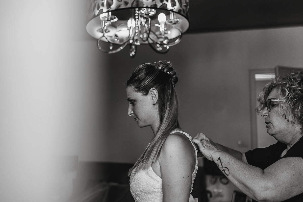 Matrimonio a Villa Sassi. Preparazione della sposa a Chieri. la parrucchiera abbottona l'abito della sposa.
