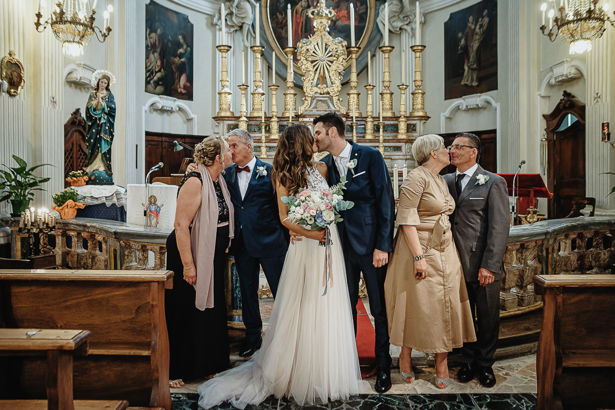 Matrimonio nella chiesa parrochiale di Arignano. Cerimonia.Foto all'altare con i genitori. Tutti si baciano.