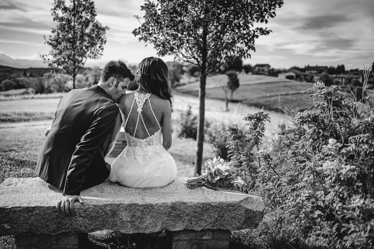 Chiesa di San Lorenzo a Mombello Torinese, sessione di coppia del matrimonio di Alice e Raffaele. Sposi seduti sulla panchina. sposo bacia la spalla della sposa.