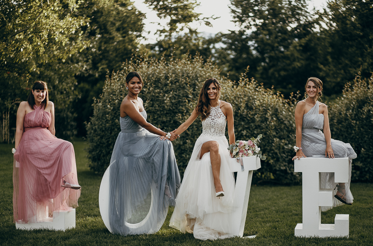 Tenuta La Michelina. Matrimonio di Alice e Raffaele. Aperitivo. Sposa con le damigelle sulla scritta LOVE