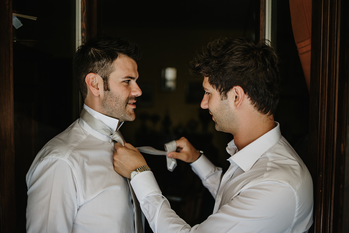 Matrimonio ad Arignano. Preparazione dello sposo.Fratello annoda la cravatta allo sposo.