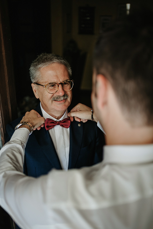 Matrimonio ad Arignano. Preparazione dello sposo.Sposo sistema il papillon al padre.