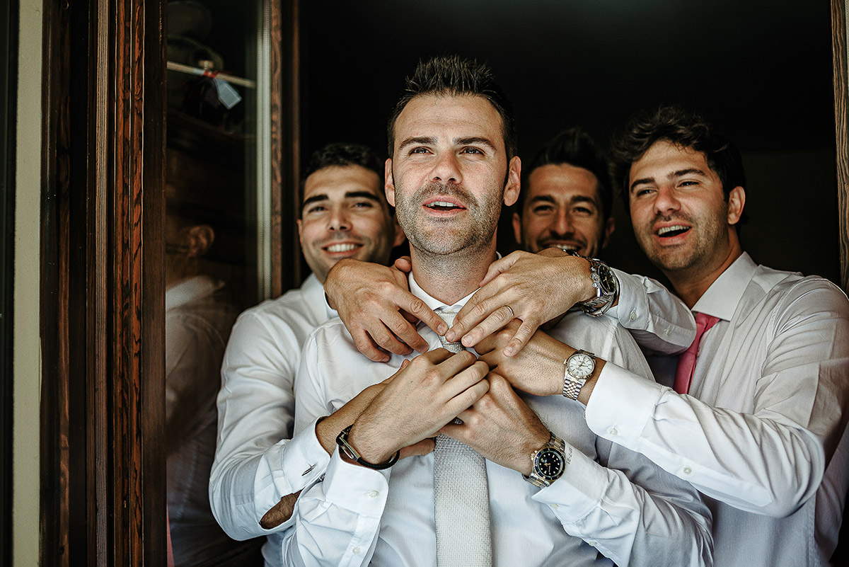 Matrimonio ad Arignano. Preparazione dello sposo.Sposo con gli amici che gli sistemano la cravatta.