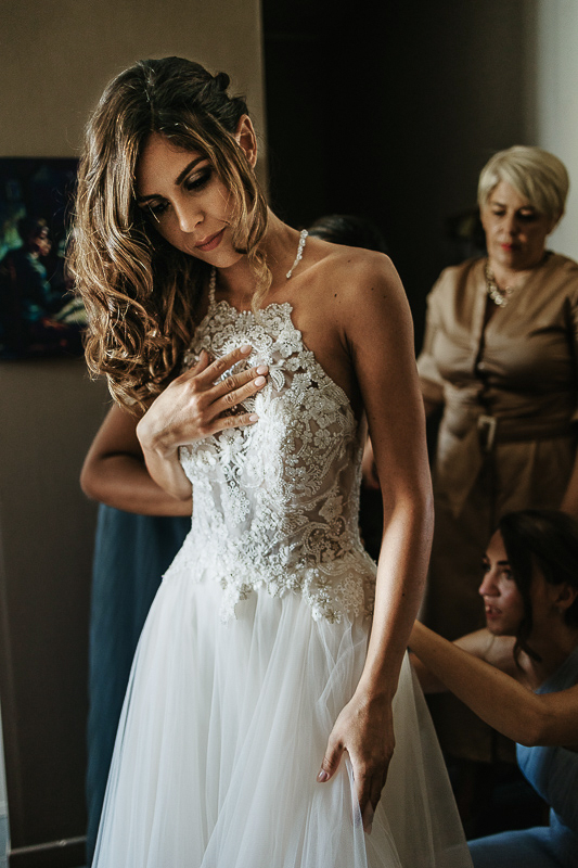 Matrimonio ad Arignano. Preparazione della sposa. Vestizione della sposa. Damigelle abbottonano l'abito.
