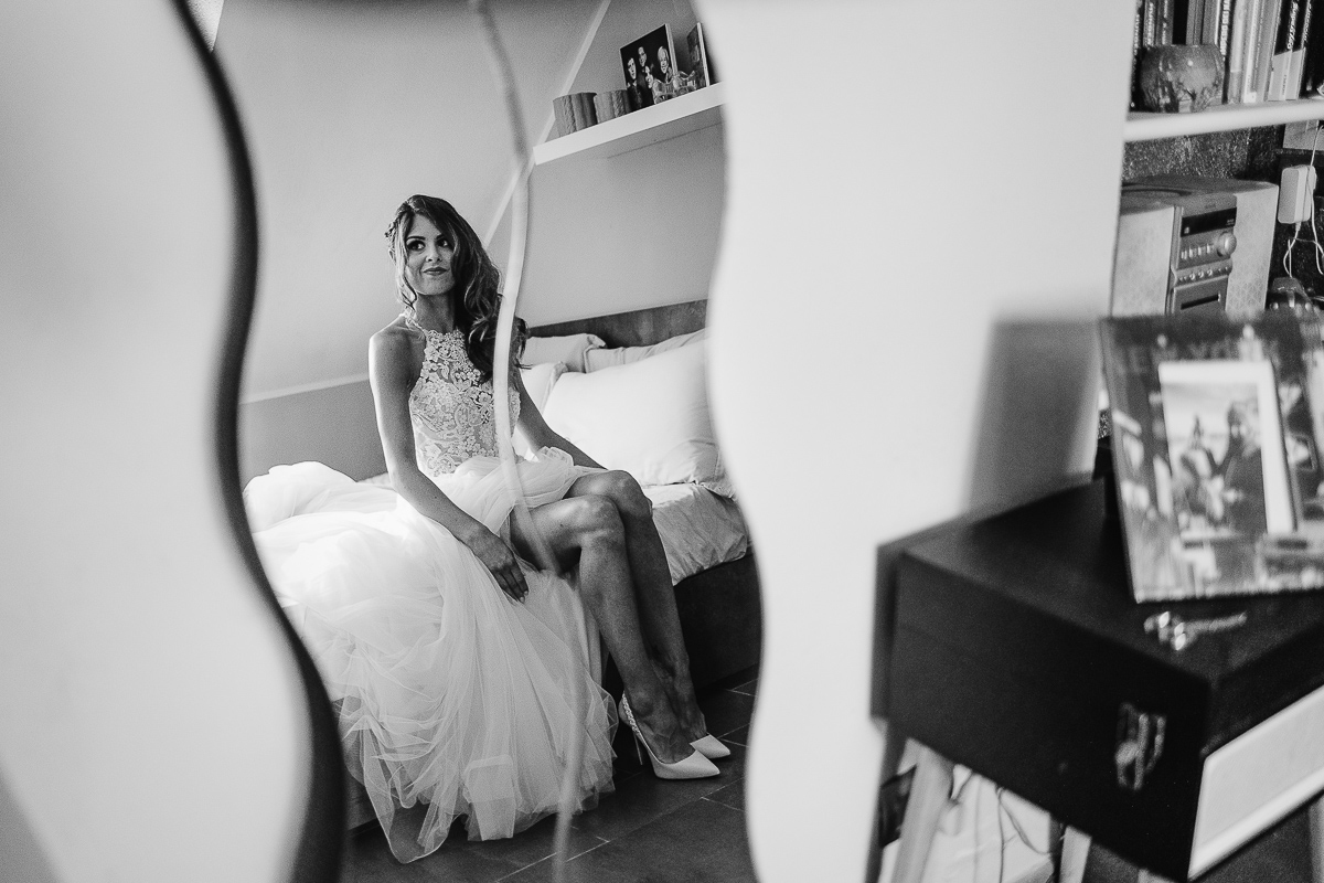 Matrimonio ad Arignano. Preparazione della sposa. Sposa seduta sul letto allo specchio.