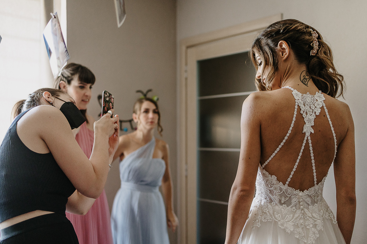 Matrimonio ad Arignano. Preparazione della sposa. Particolare della schiena della sposa. MUA che fa una foto con il cellulare.