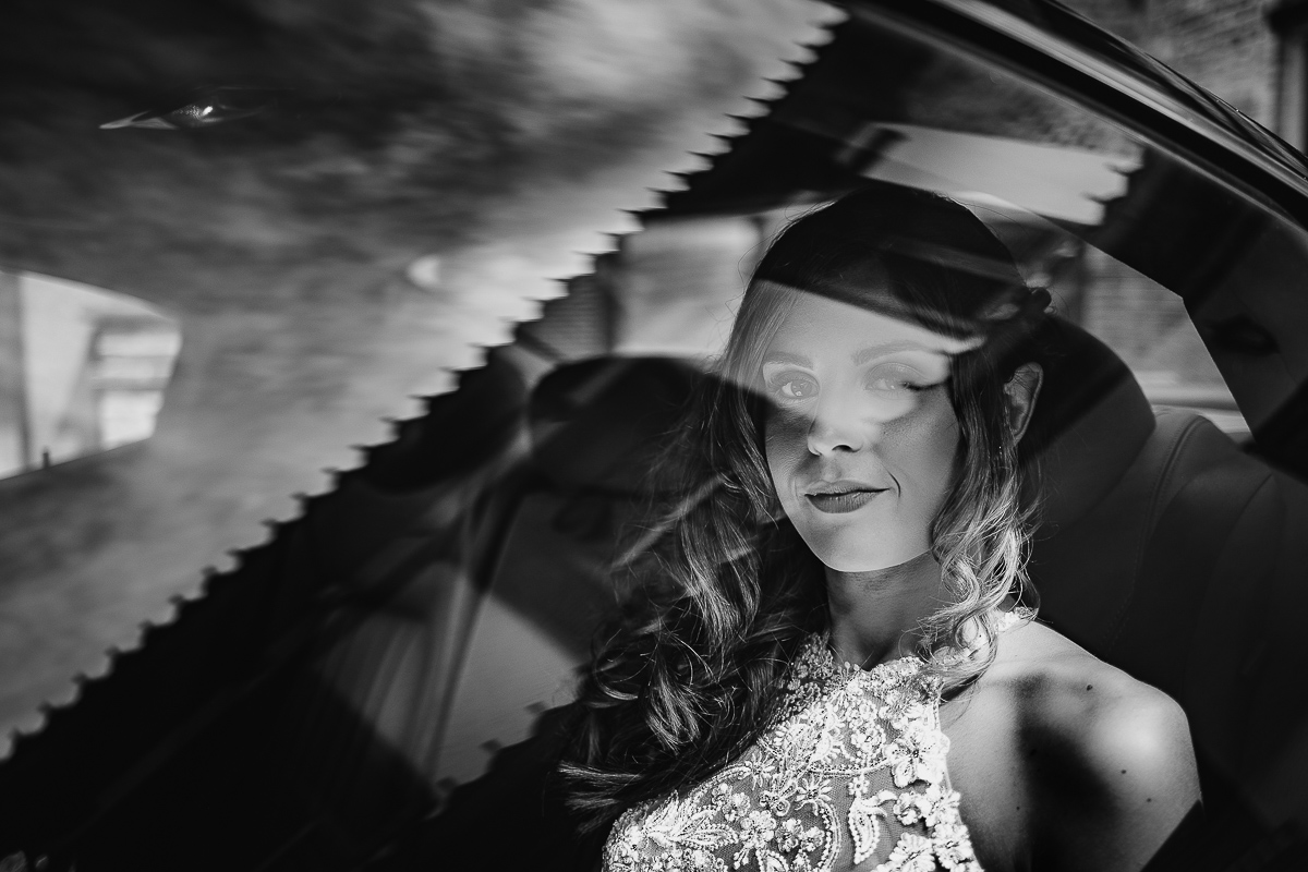 Matrimonio ad Arignano. Preparazione della sposa. Sposa in auto riflessa dal vetro del finestrino.