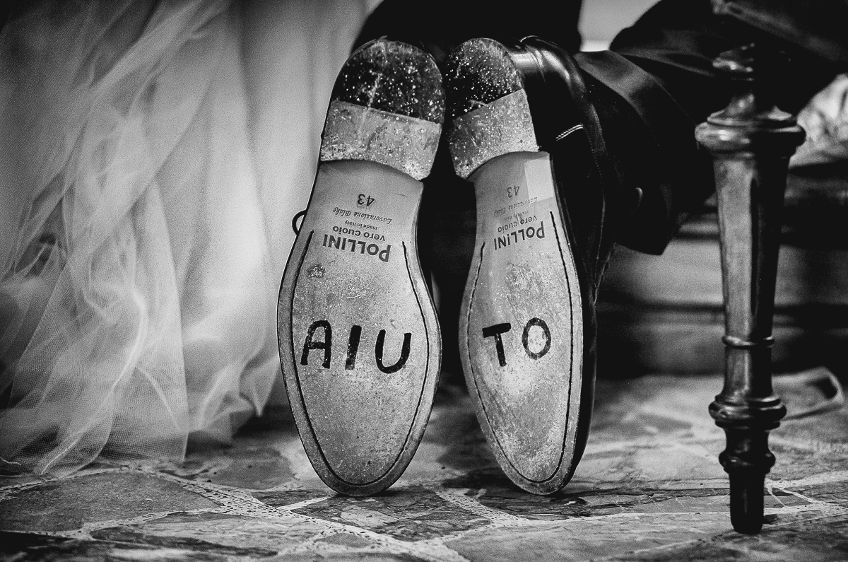 Matrimonio nella chiesa parrochiale di Arignano. Cerimonia. Scarpe dello sposo inginocchiato. Sulle suole è presente la scritta. AIUTO