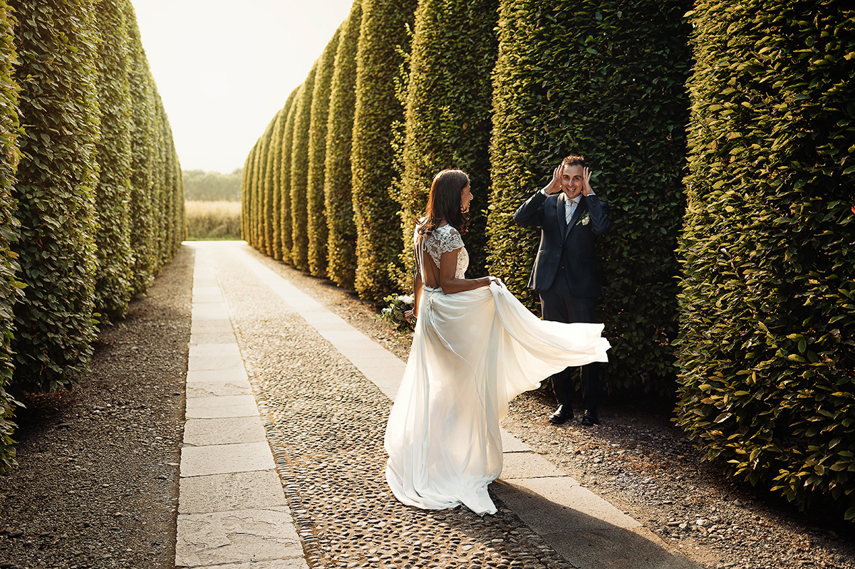 Tenuta La Cascinetta di Buriasco. Matrimonio. Sessione di coppia al tramonto lungo il viale di cipressi. Sposa che danza davanti allo sposo con le mani sugli occhi.