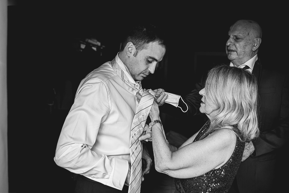Tenuta La Cascinetta di Buriasco. Matrimonio. Preparazione dello sposo. Mamma aiuta lo sposo nella vestizione. padre guarda.