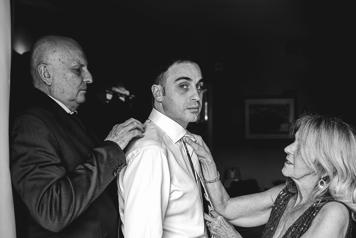 Tenuta La Cascinetta di Buriasco. Matrimonio. Preparazione dello sposo. Sposo con i genitori che lo aiutano nella vestizione.