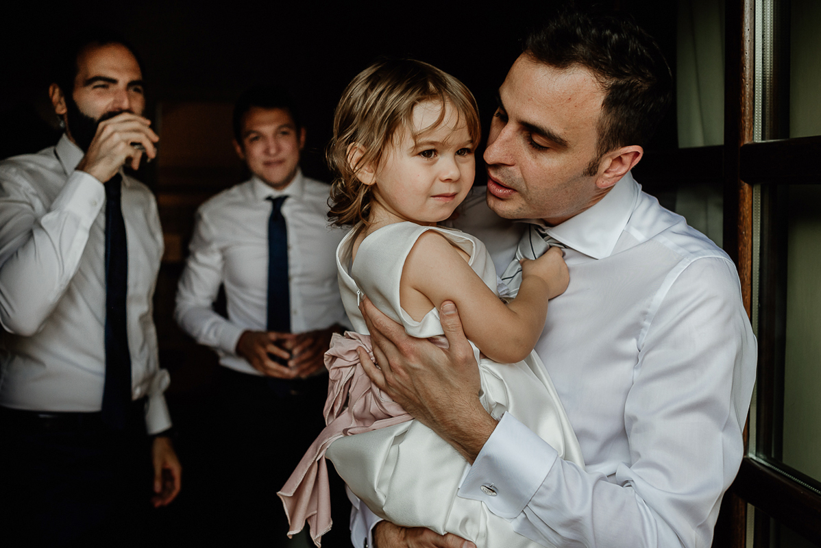 Tenuta La Cascinetta di Buriasco. Matrimonio. Preparazione dello sposo. Sposo con la sua bambina in braccio e testimoni sullo sfondo.