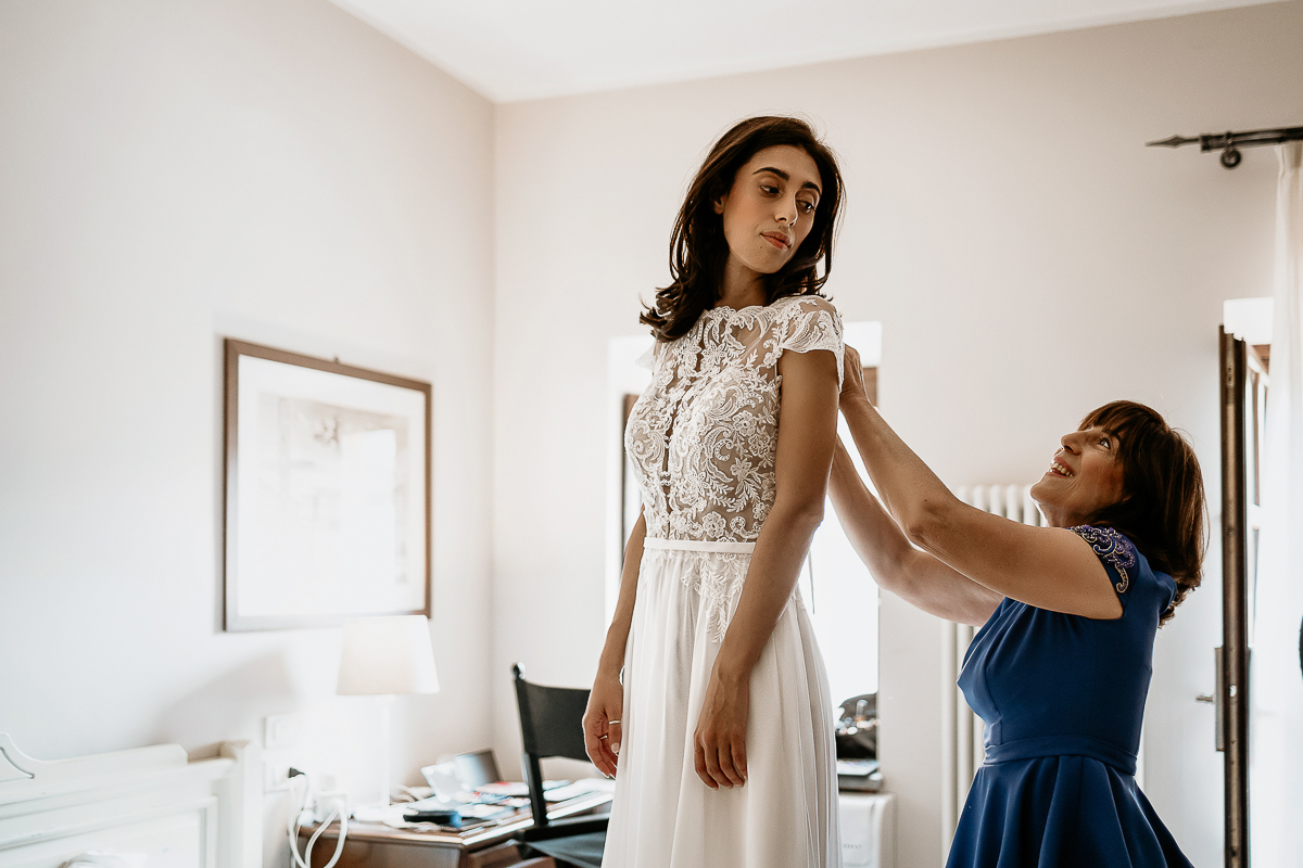 Tenuta La Cascinetta di Buriasco. Matrimonio. Preparazione della sposa. mamma lega il fiocco sulla schiena della sposa
