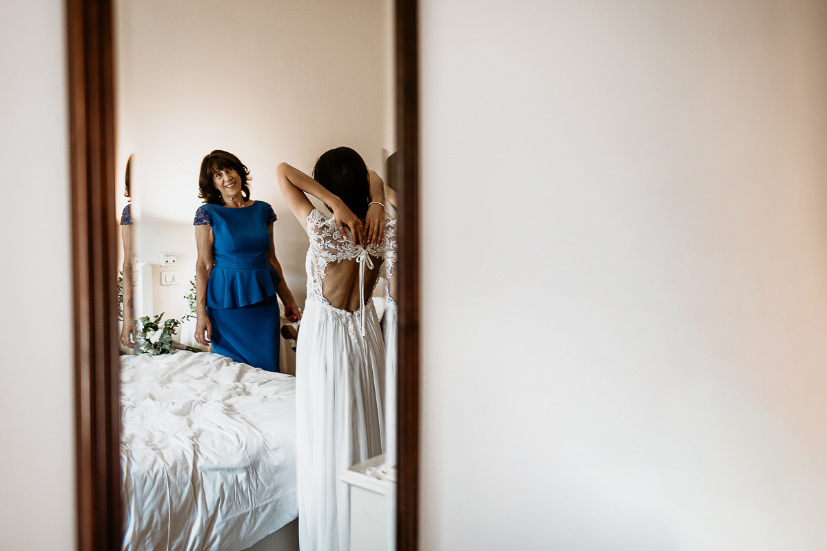 Tenuta La Cascinetta di Buriasco. Matrimonio. Preparazione della sposa. Sposa controlla il fiocco sul retro del suo abito.