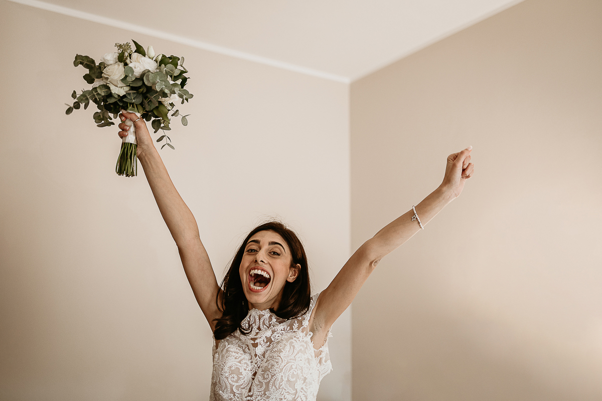 Tenuta La Cascinetta di Buriasco. Matrimonio. Preparazione della sposa. Sposa fa una scena di giubilo con il bouquet levato al cielo.