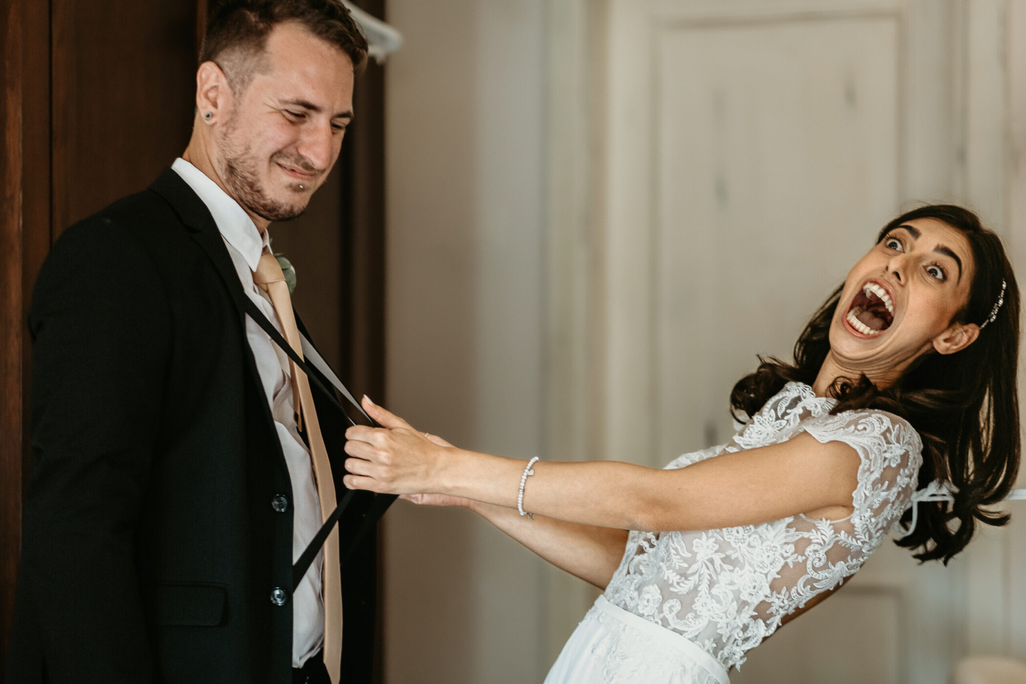Tenuta La Cascinetta di Buriasco. Matrimonio. Preparazione della sposa. Sposa tira le bretelle ad un testimone.