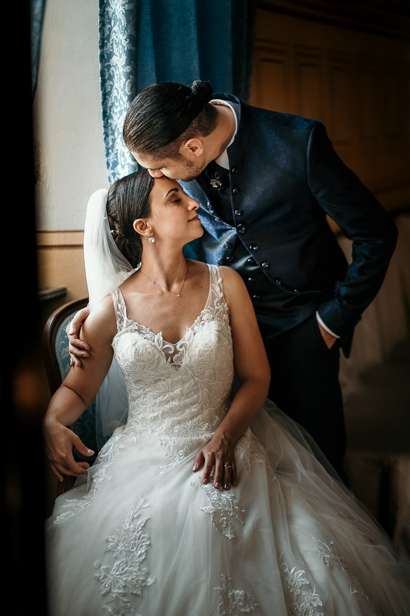 Castello di Cortanze, matrimonio. Ricevimento. Sposo bacia la sposa seduta sulla fronte
