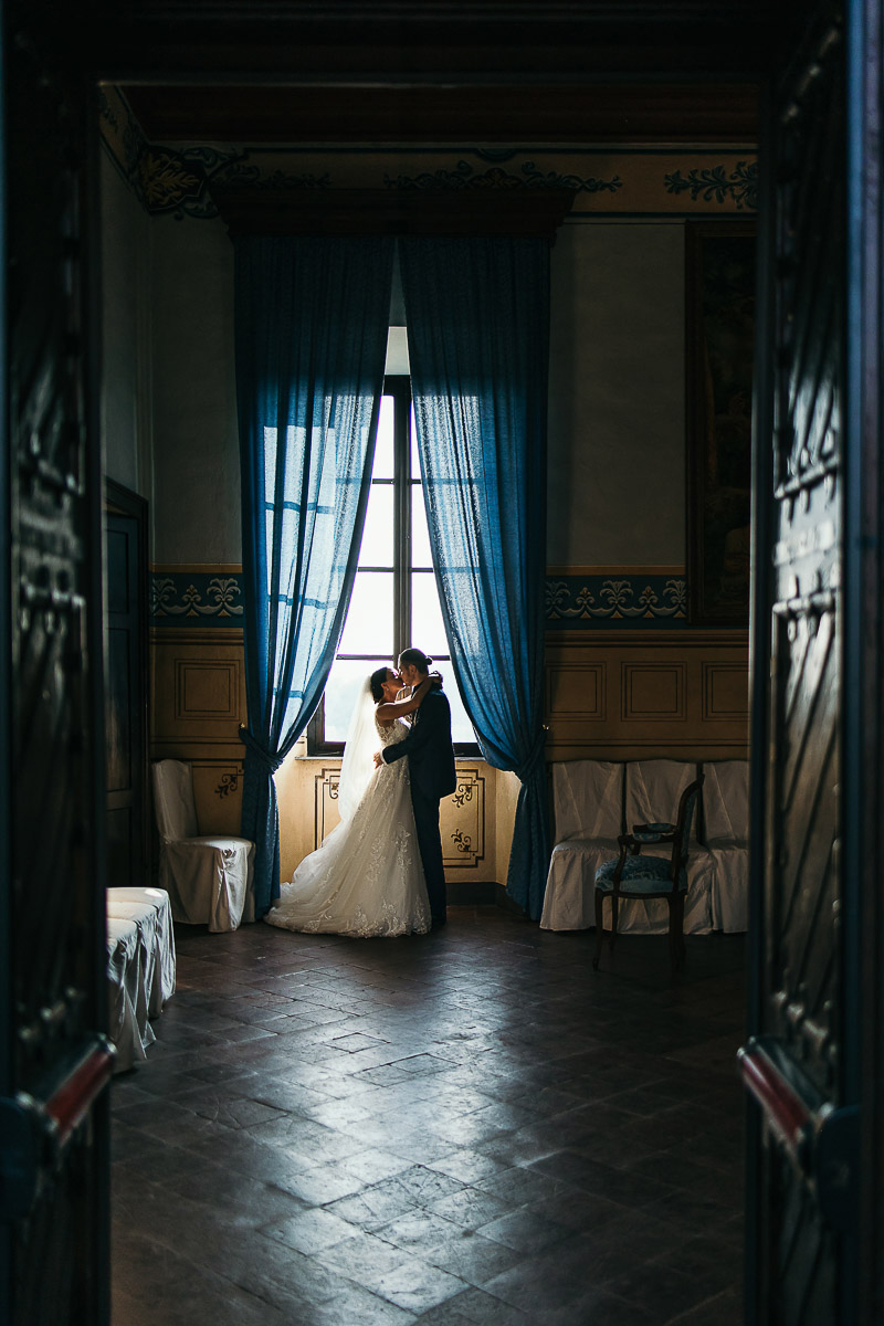 Castello di Cortanze, matrimonio. Ricevimento.Ritratto degli sposi davanti alla finestra. Bacio