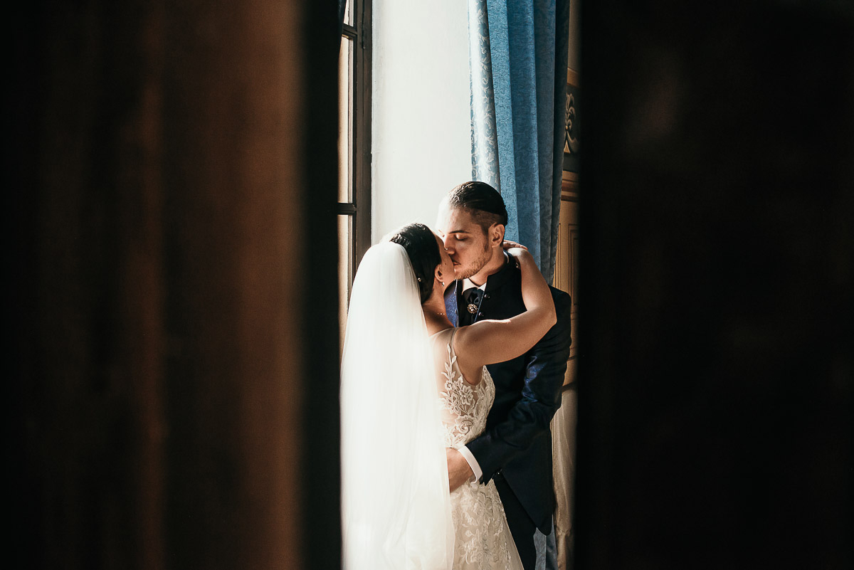 Castello di Cortanze, matrimonio. Ricevimento.Ritratto degli sposi davanti alla finestra. Bacio