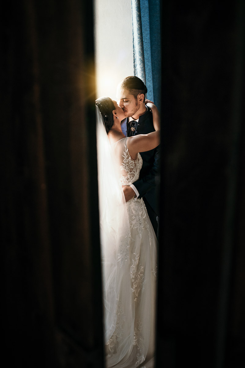 Castello di Cortanze, matrimonio. Ricevimento. Bacio degli sposi davanti alla finestra tra i tendaggi