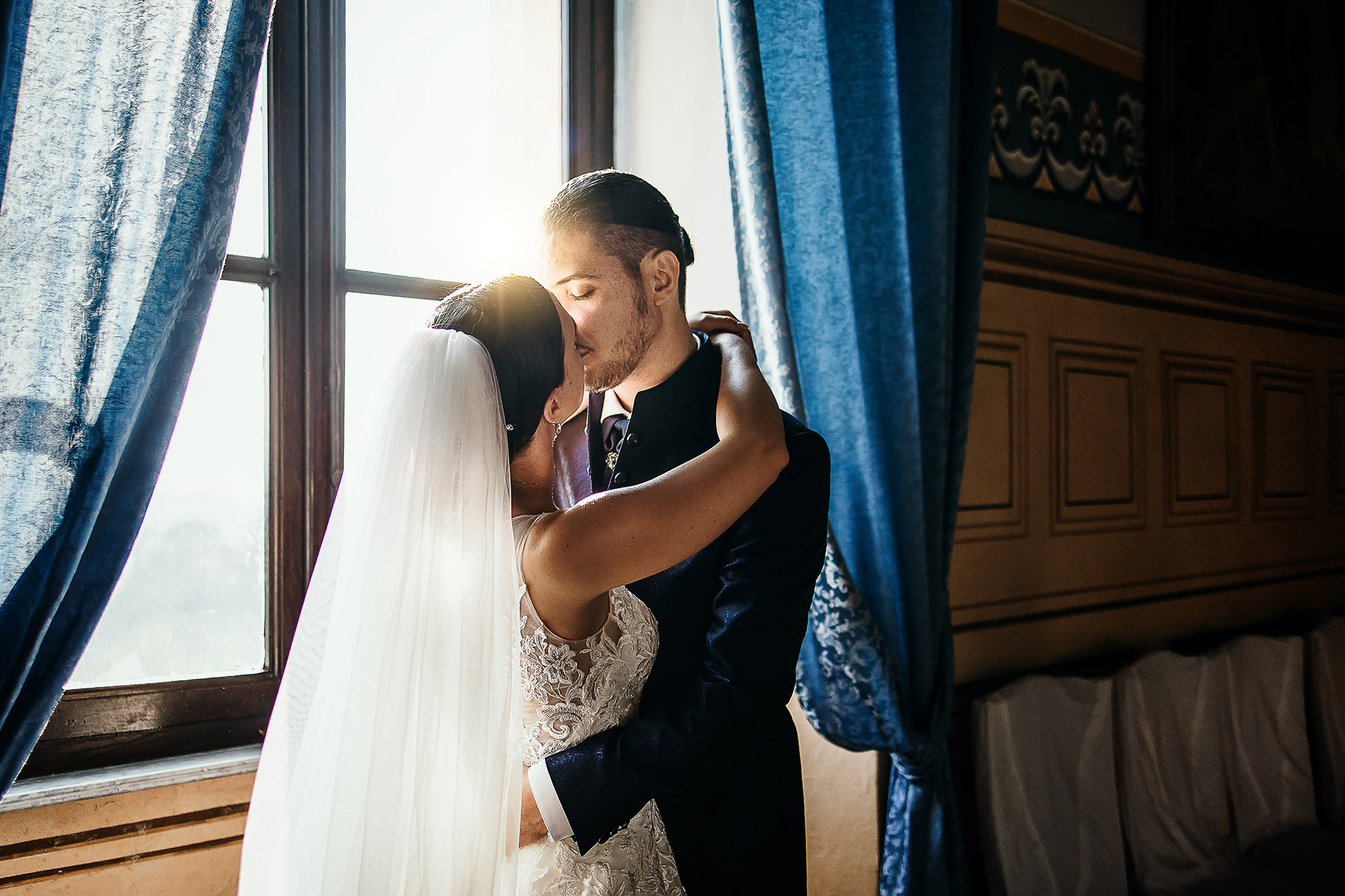 Matrimonio al Castello di Cortanze. Bacio degli sposi davanti alla finestra in una sala del castello con il sole che li illumina dalla finestra.