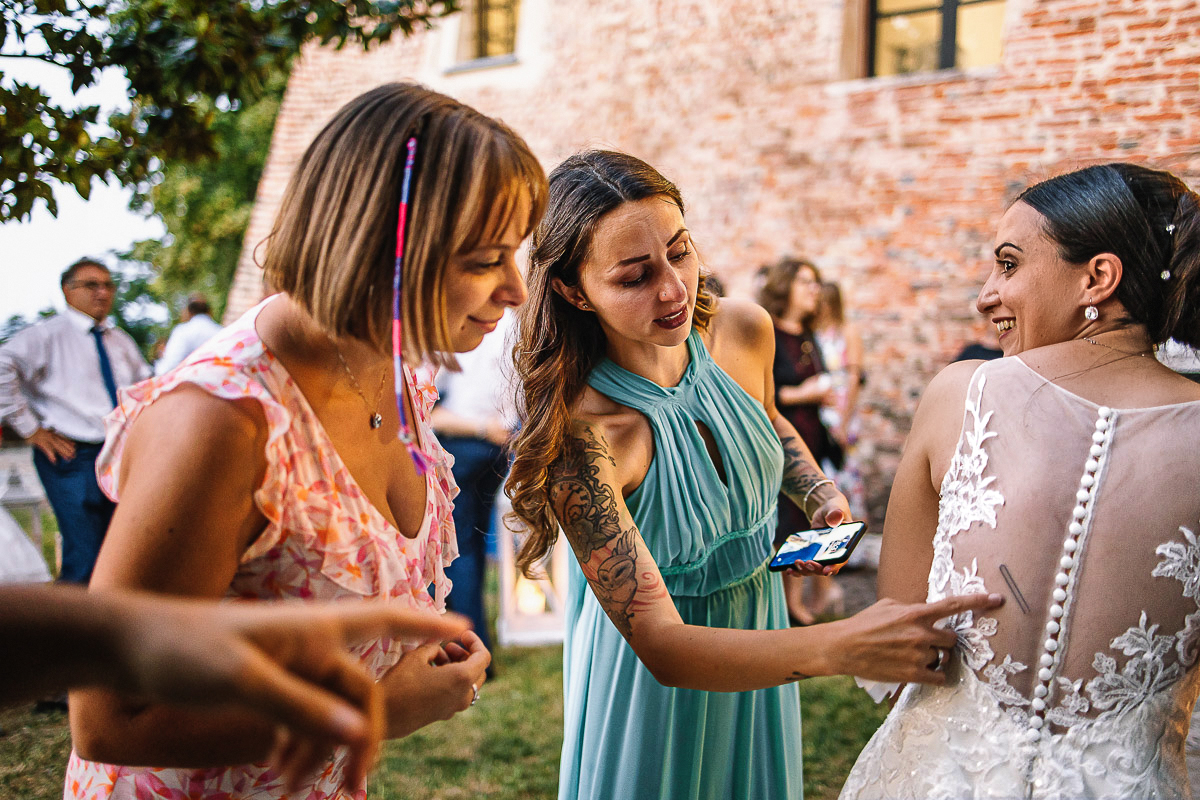 Castello di Cortanze, matrimonio. Ricevimento. amiche cercano di togliere una clip dalla schiena della sposa.