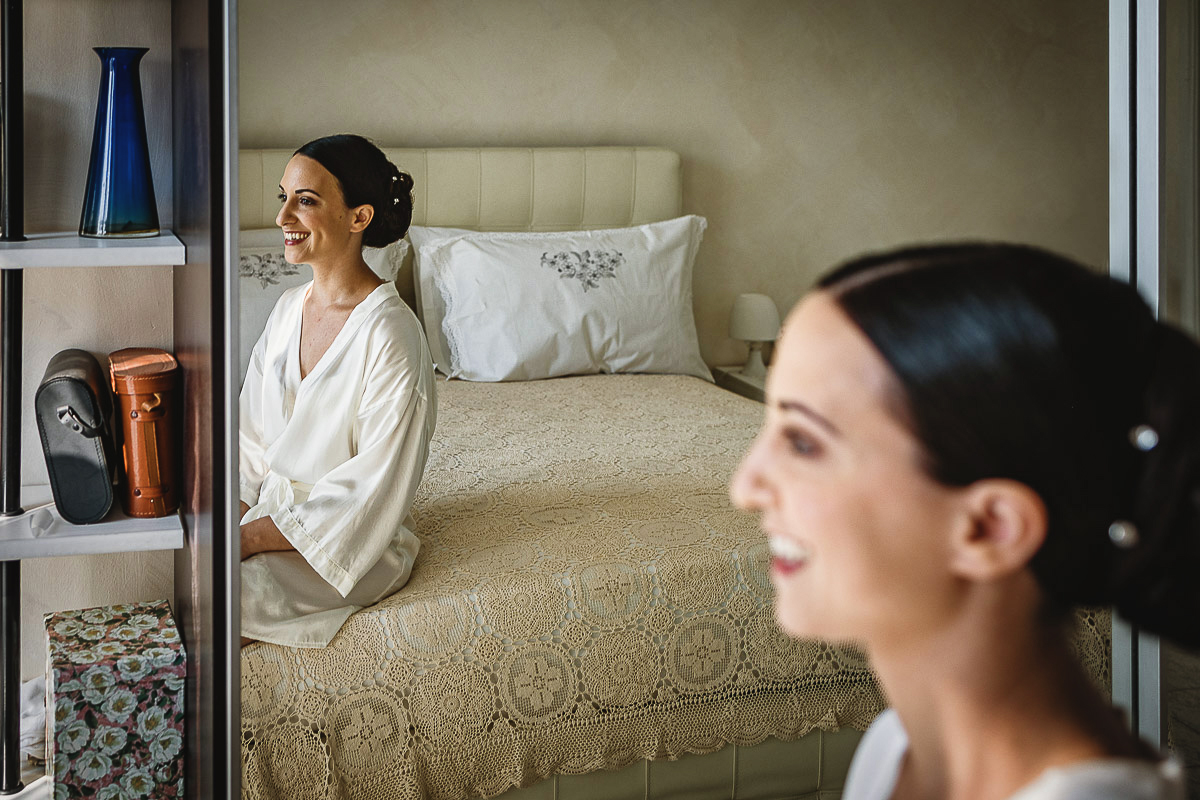 Matrimonio a Torino, preparazione della sposa, sposa seduta sul letto riflessa nello specchio dell'armadio