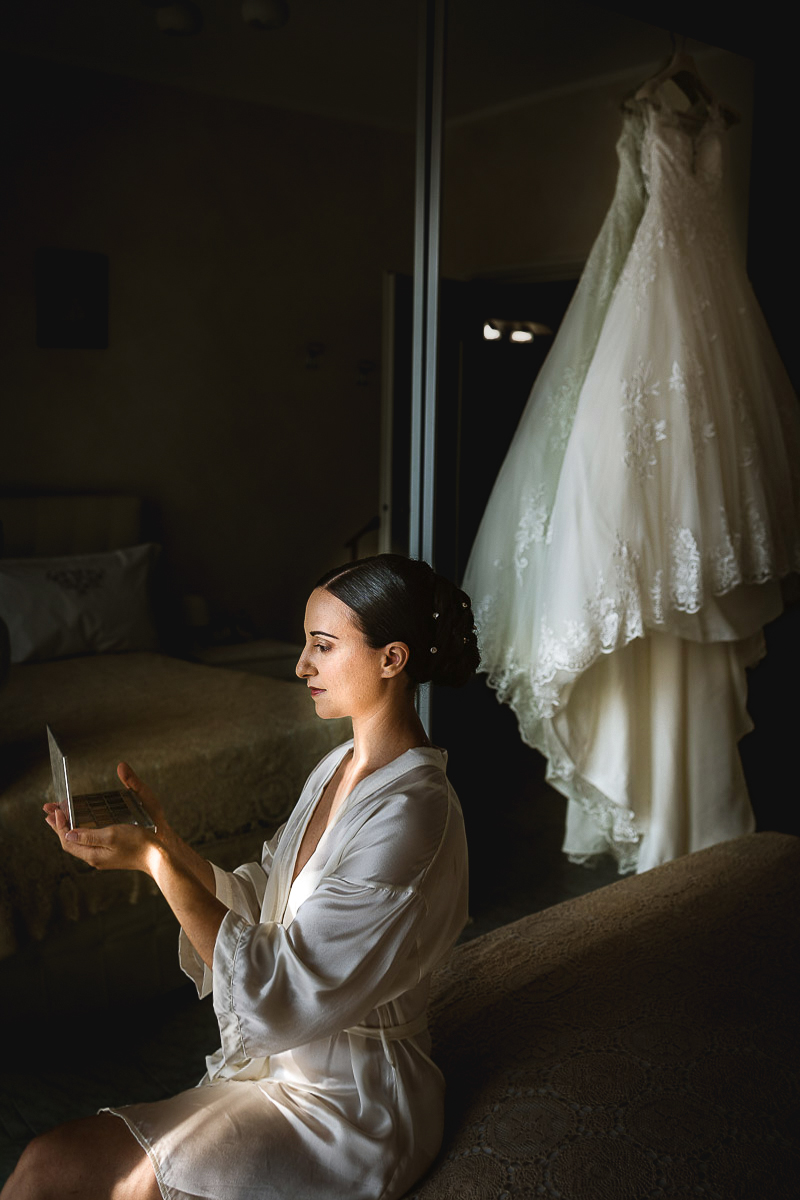 Matrimonio a Torino, preparazione della sposa, Make-up- Sposa con la palette degli ombretti. abito appeso dietro di lei.