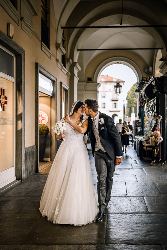 Matrimonio a Torino. Sessione di coppia davanti alla stazione di Porta Nuova. Sposi si baciano camminando sotto i portici di Corso vittorio Emanuele.