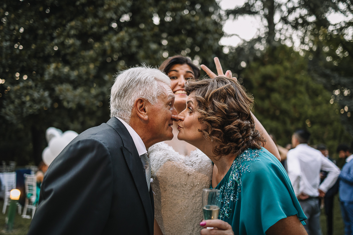 matrimonio al Castello di Oviglio. Aperitivo. Bacio dei genitori e sposa che ride dietro.