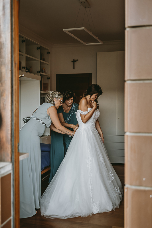 Matrimonio a Torino, preparazione della sposa. Mamma e amica abbottonano l'abito alla sposa.
