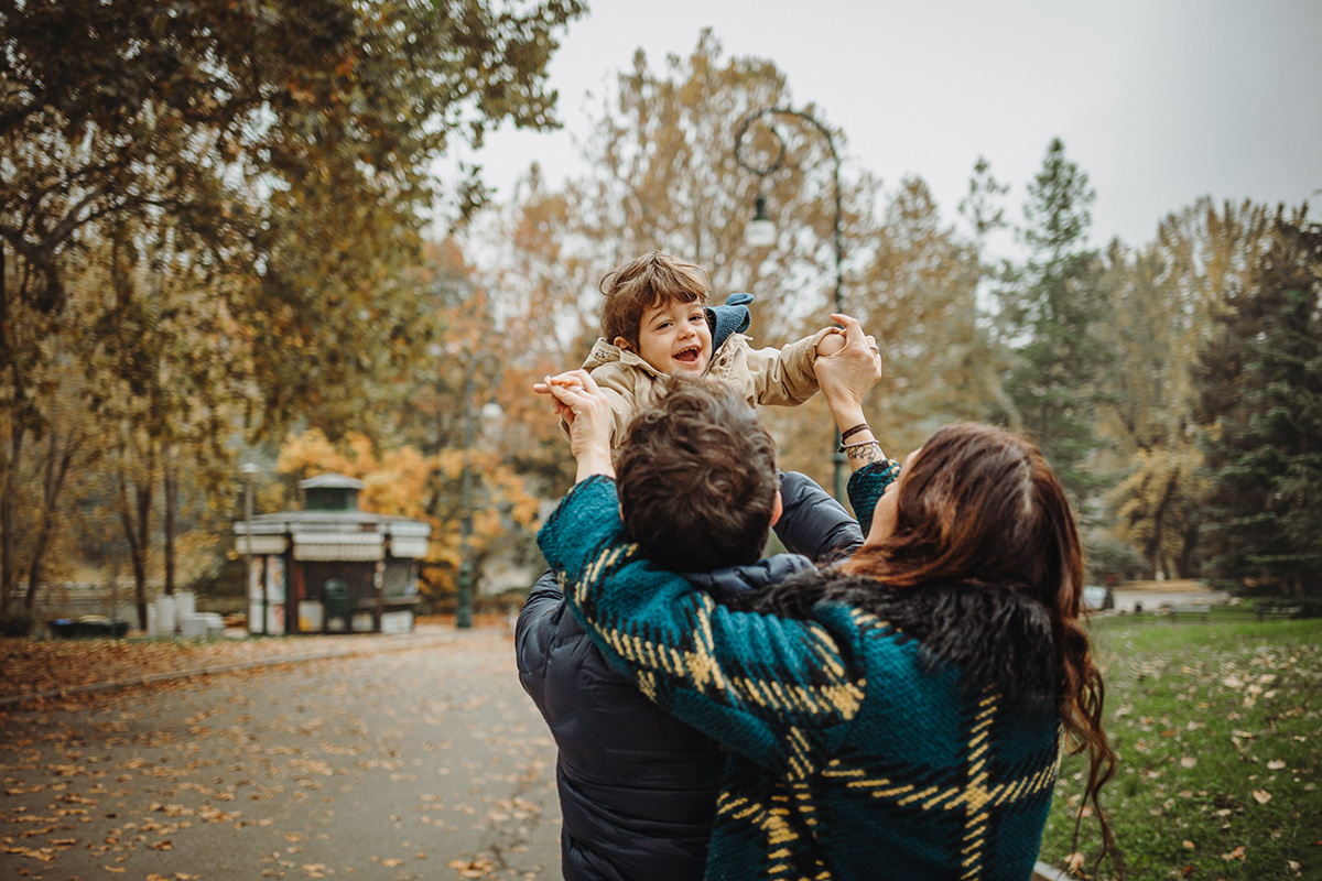 Parco del Valentino, fotografia di famiglia. Sessione fotografica autunnale. Papà e mamma fanno volare il bambino di fronte a loro.