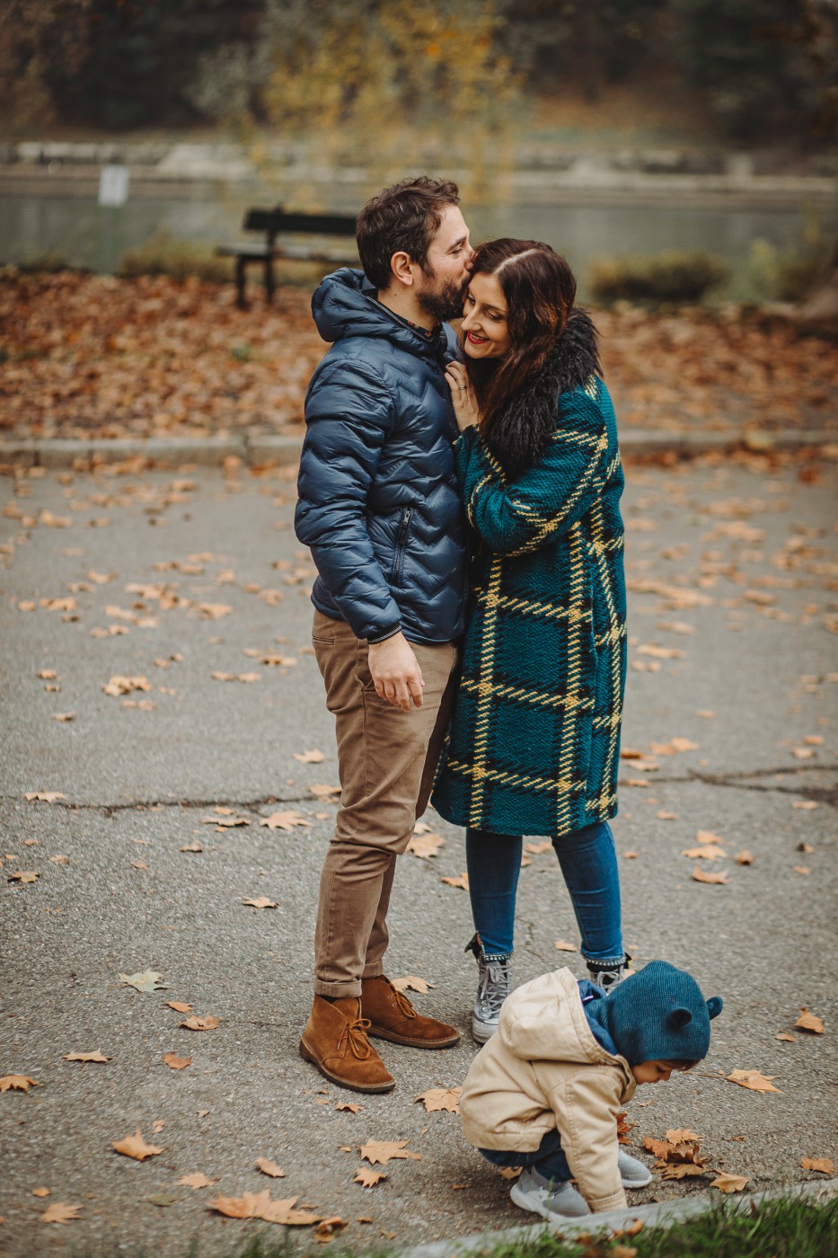 Parco del Valentino, fotografia di famiglia. Sessione fotografica autunnale. Papà e mamma insieme e bambino gioca davanti a loro.